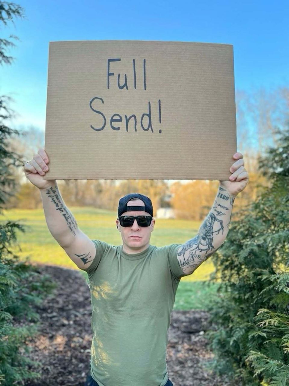 Military-connected creator holding a hand-lettered sign outdoors
